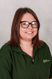 Nursery worker with brown hair and glasses wearing green polo shirt.