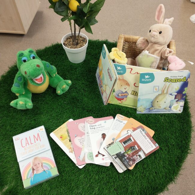 Child's soft toys, story books, and ornamental tree on green grass-effect rug.