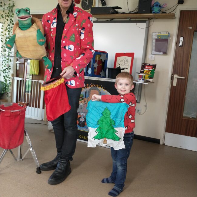 Infant child with Christmas tree picture, by children's entertainer with turtle glove puppet.