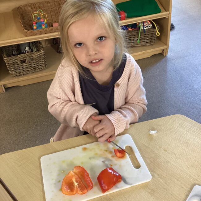 Infant girl chopping fruit on chopping board at nursery.