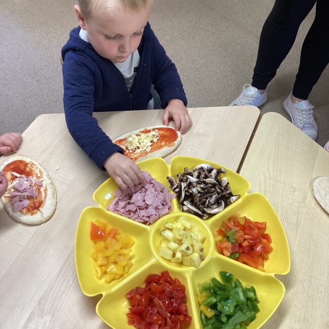 Infant boy taking food from food platter at nursery.