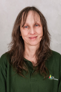 Female nursery worker with dark hair wearing green polo shirt.