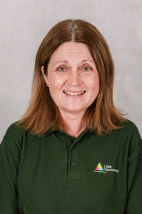 Female nursery worker with light brown hair wearing green polo shirt.